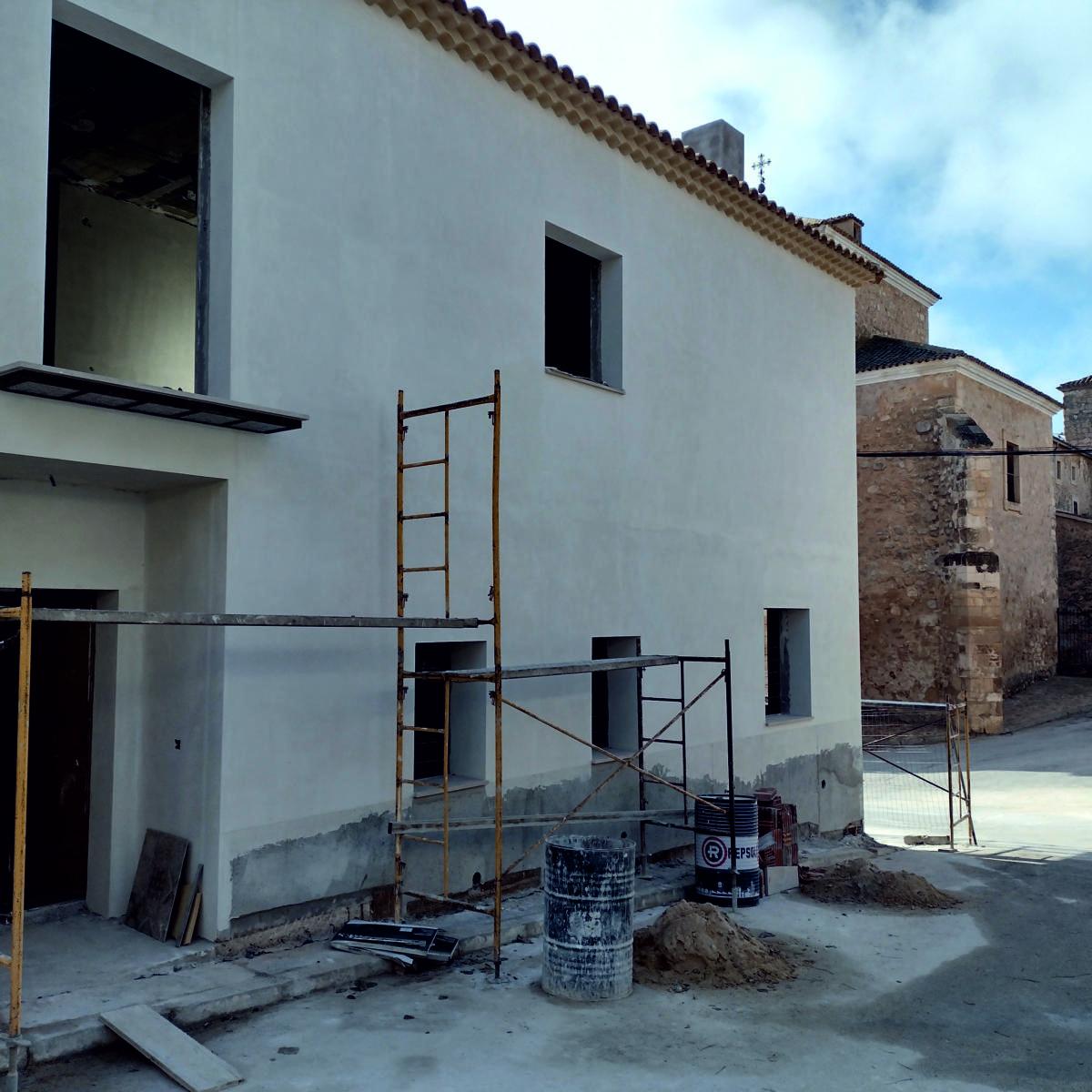 Vista exterior en construcción. Fachada blanca con cubierta de teja tradicional junto a la iglesia histórica.